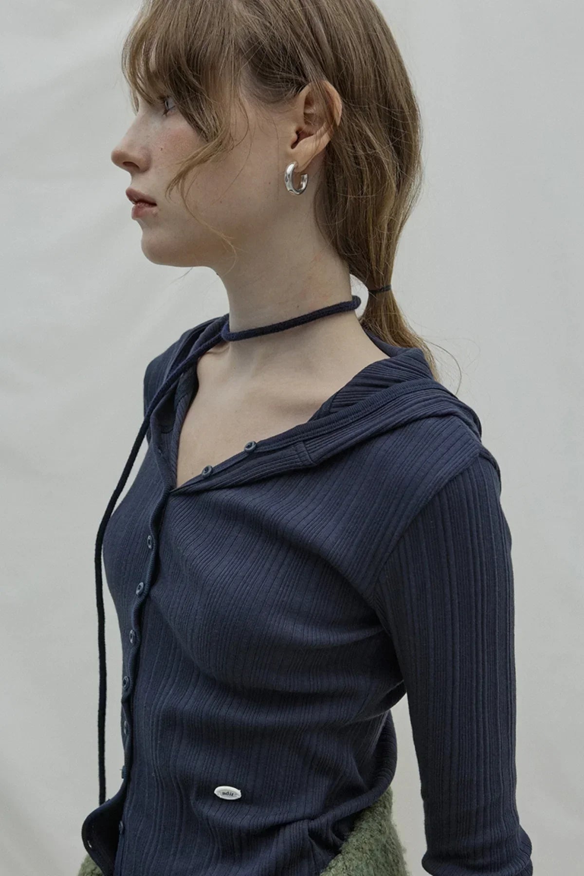 Profile of woman wearing navy ribbed hooded cardigan with buttons and silver hoop earrings