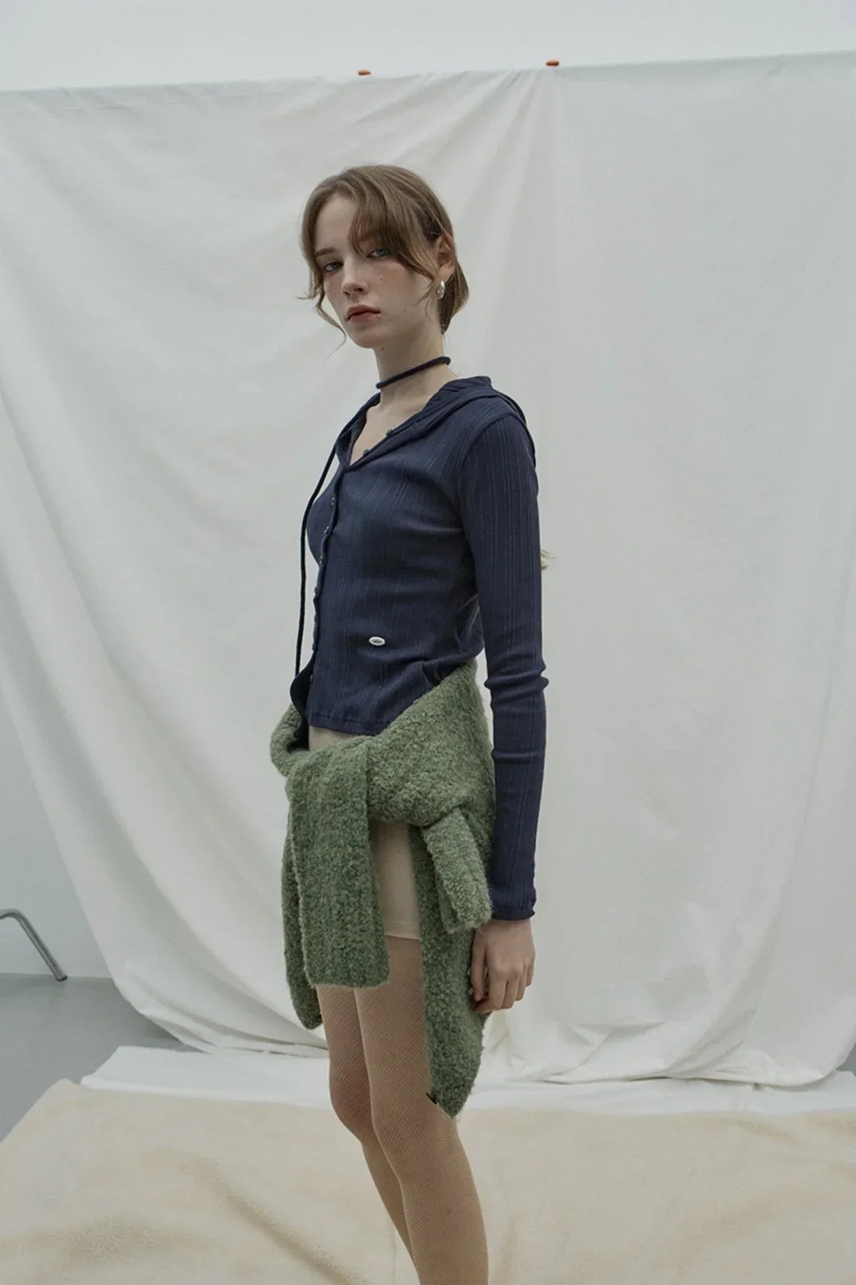 Woman wearing navy ribbed button-up hooded cardigan with green knit sweater tied around waist in studio