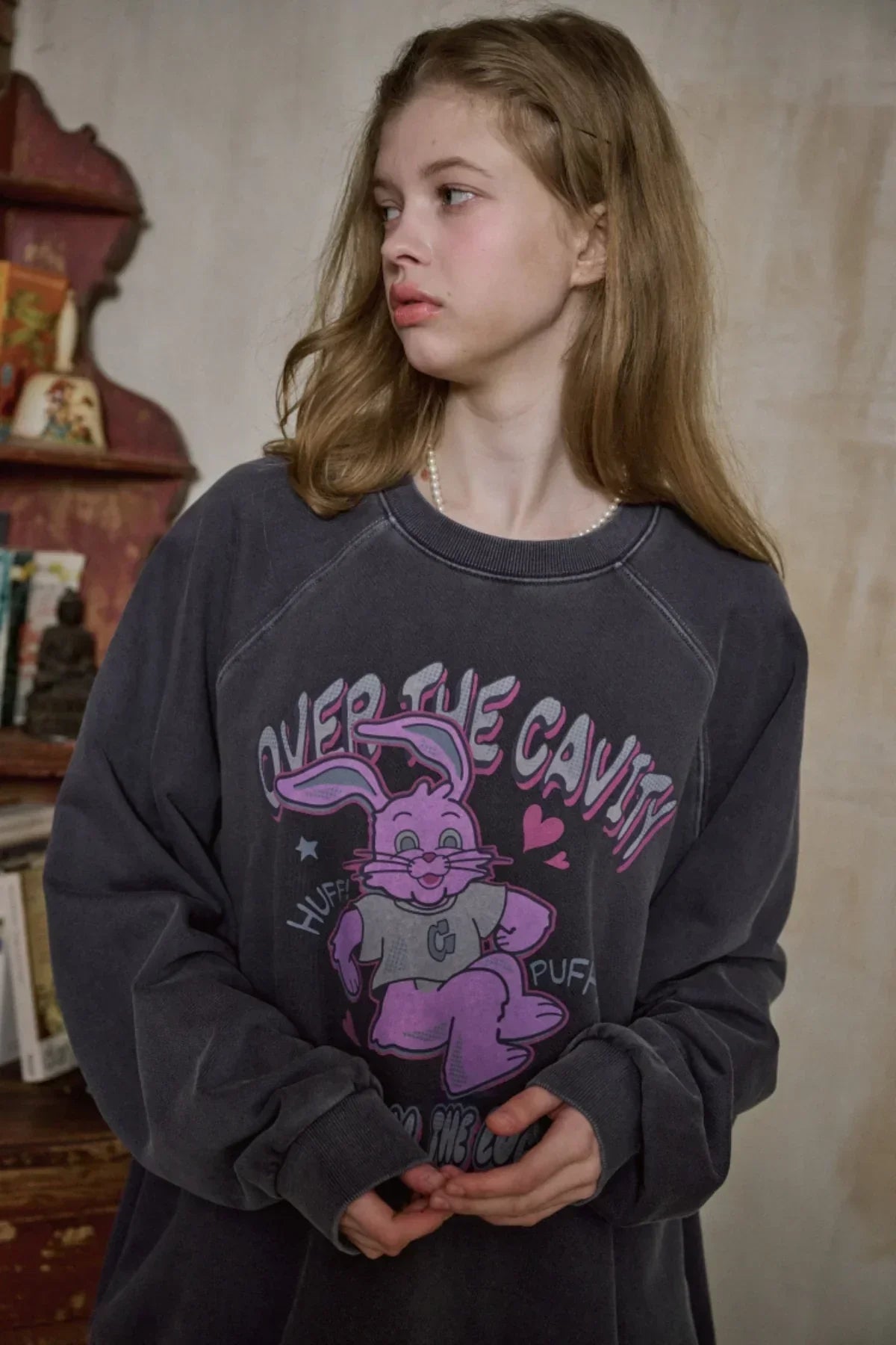 Young woman wearing dark blue raglan sweatshirt with pink cartoon bunny and text, indoor vintage setting