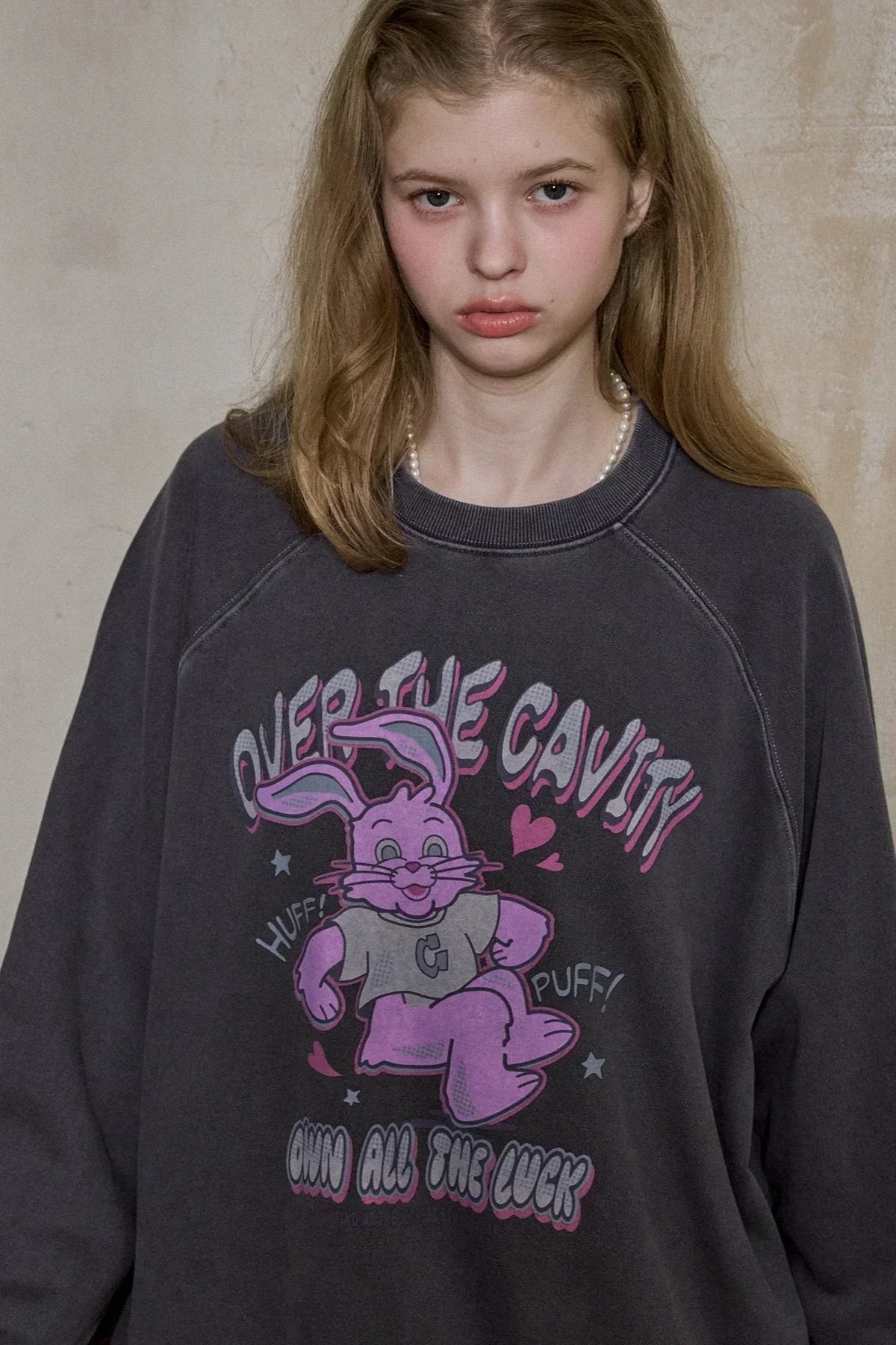 Young woman wearing dark blue sweatshirt with pink cartoon bunny and text design