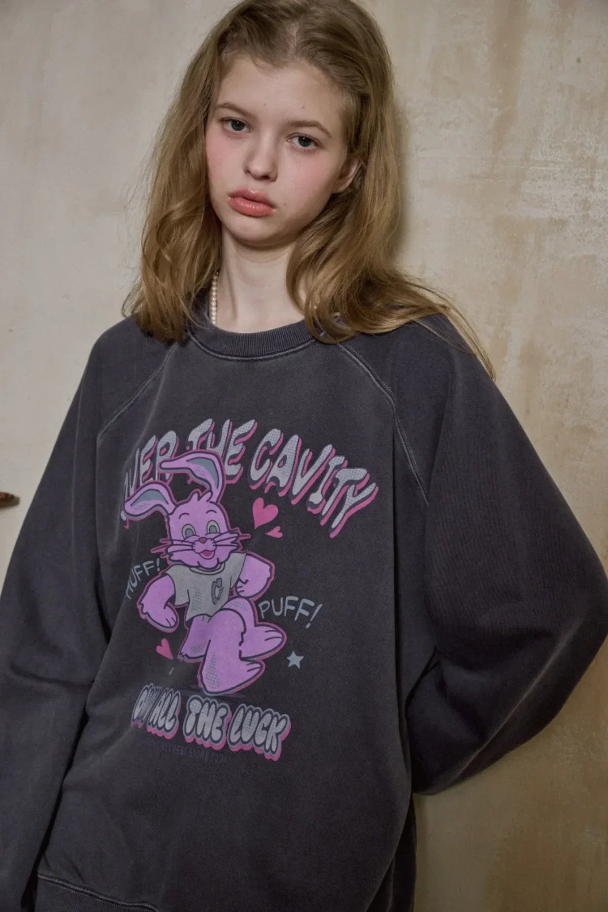 Young woman wearing dark blue raglan sweatshirt with pink cartoon bunny and cavity theme graphic