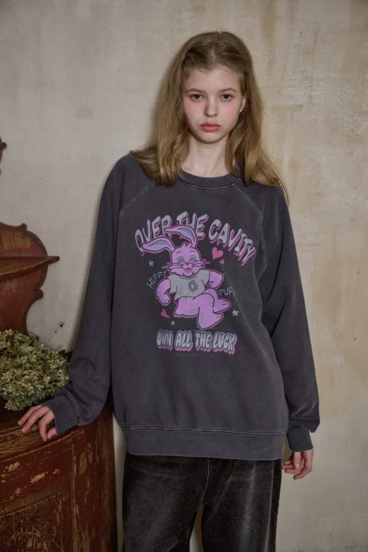 Young woman wearing dark blue oversized raglan sweatshirt with pink cartoon bunny graphic indoors