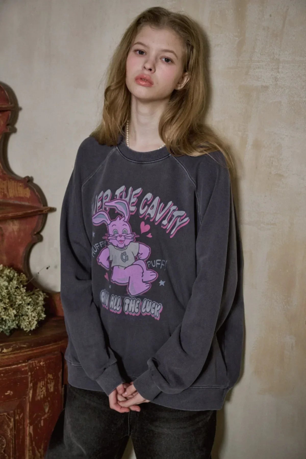 Young woman in dark blue vintage raglan sweatshirt with pink cartoon rabbit graphic, standing indoors
