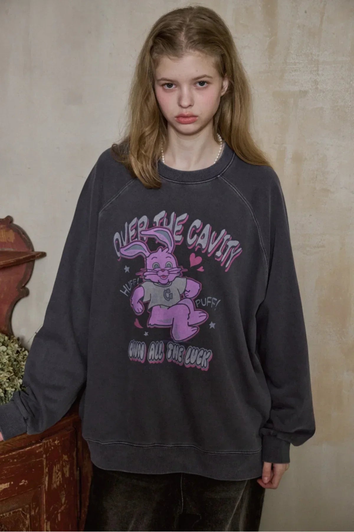 Young woman wearing dark blue oversized sweatshirt with pink cartoon rabbit and text in a rustic interior