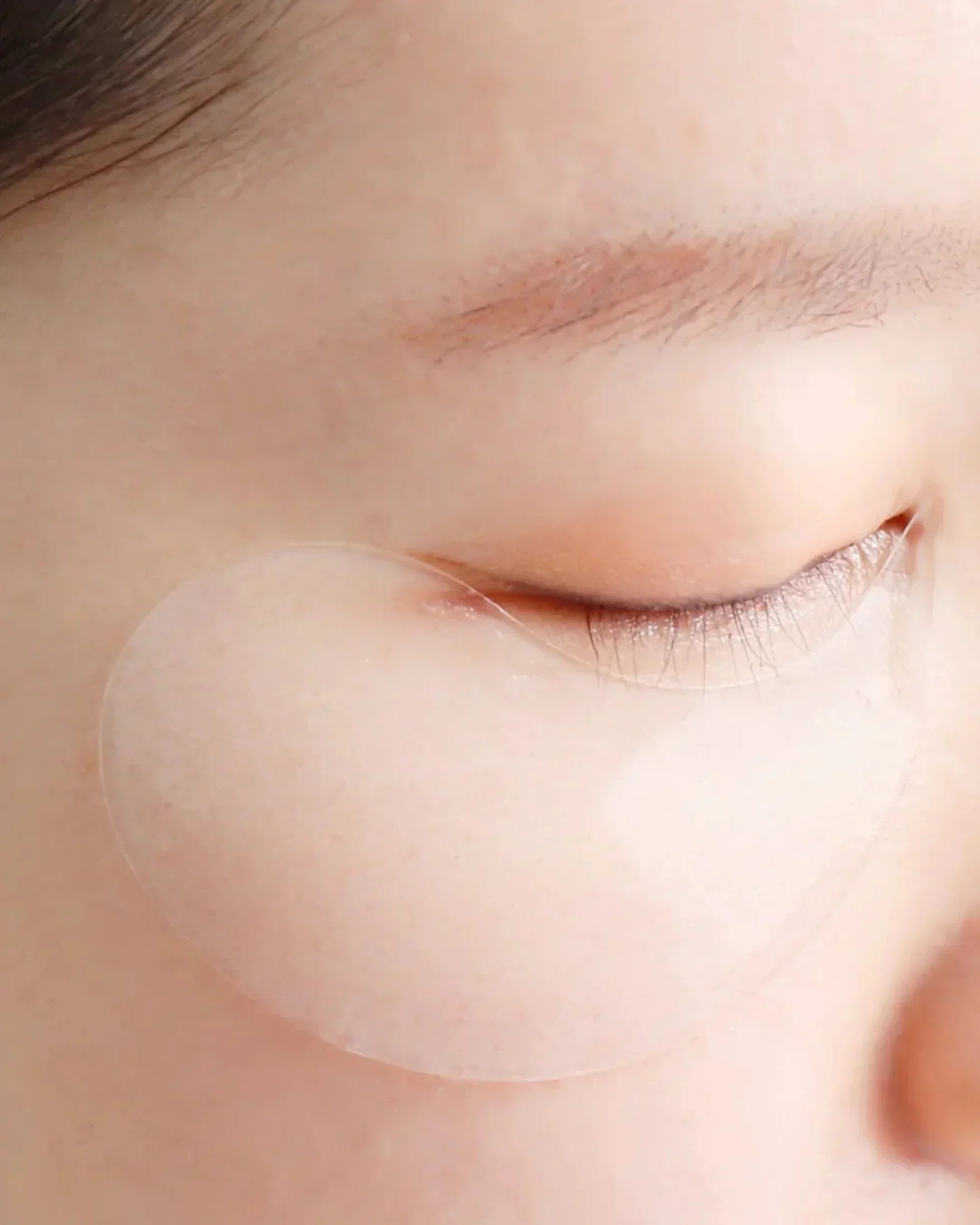 Close-up of closed eye with translucent hydrogel eye mask under eye on smooth skin
