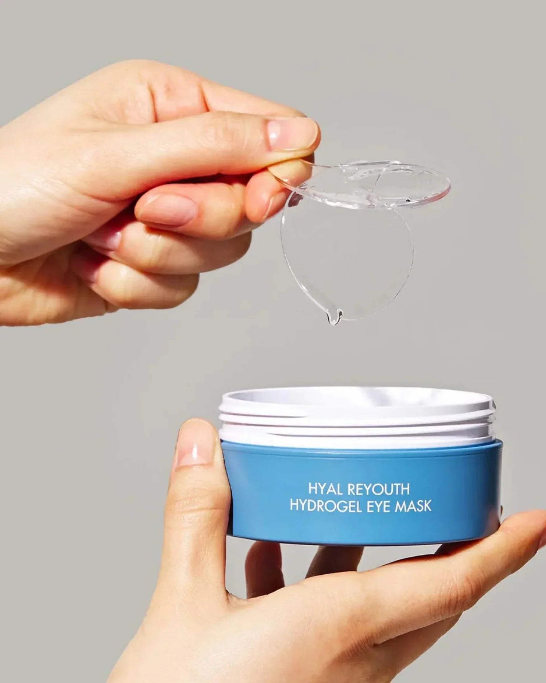 Hand holding translucent hydrogel eye mask above open blue container labeled Hyal Reyouth Hydrogel Eye Mask