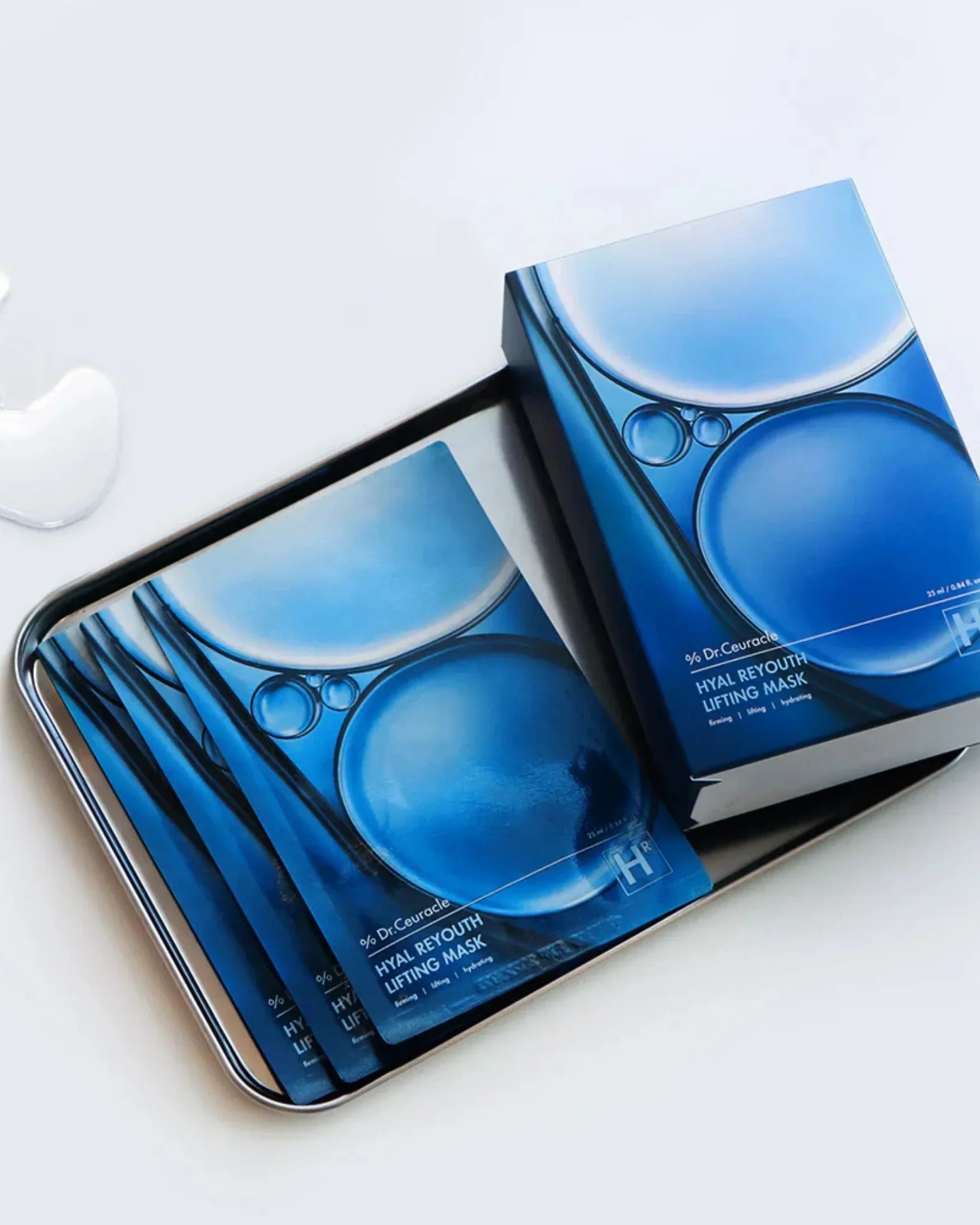 Dr. Ceuracle Hyal Reyouth Lifting Mask packets and box on a silver tray, blue skincare packaging