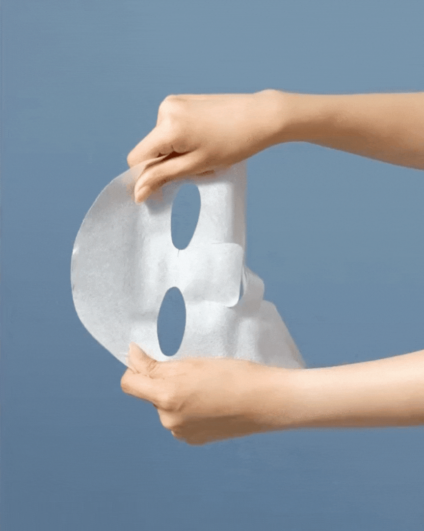 Hands holding and stretching a white facial sheet mask against a blue background