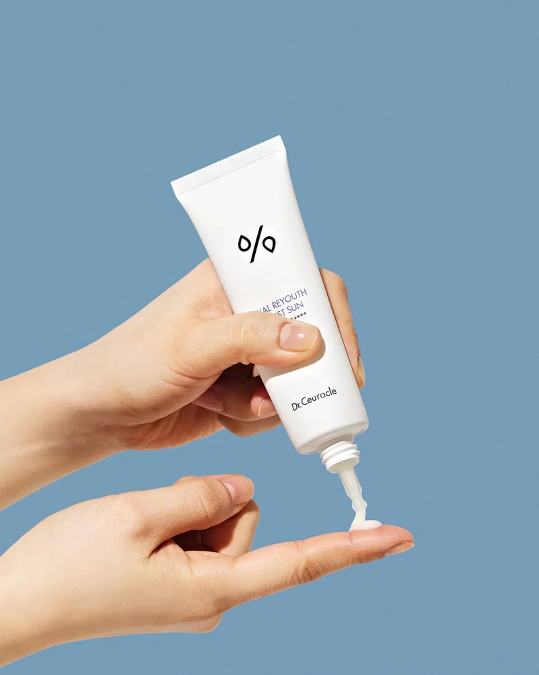Hand squeezing Dr.Ceuracle Hyal Reyouth Moist Sun sunscreen cream on fingertip against blue background