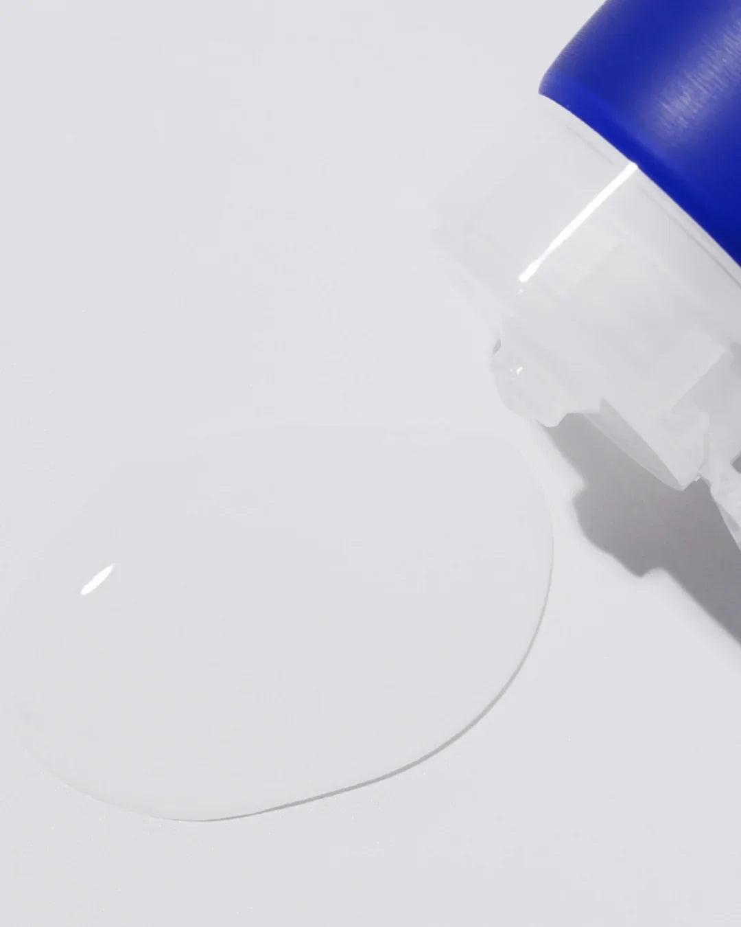 Close-up of clear hyaluronic acid gel being dispensed from a blue-capped transparent bottle on a white surface