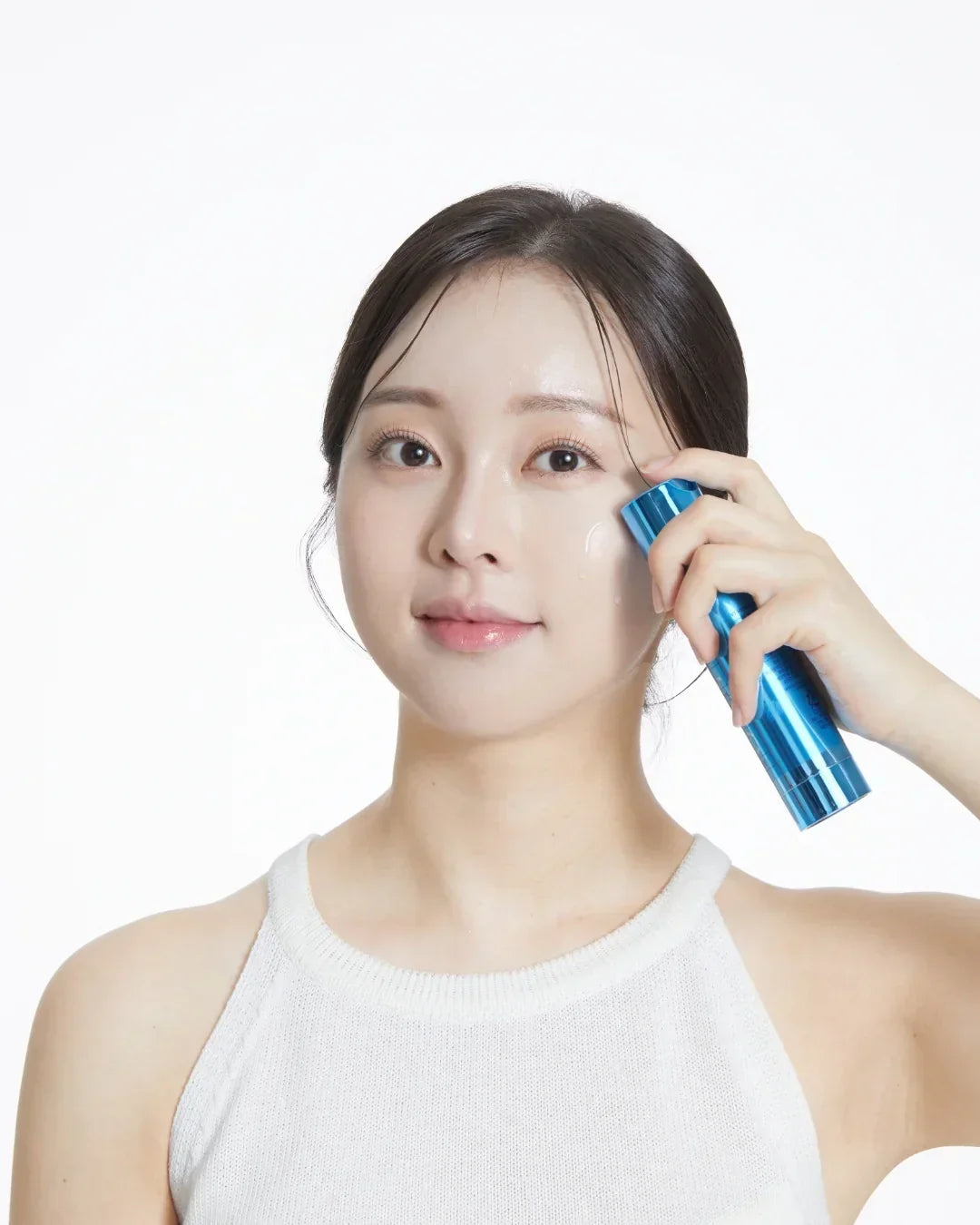 Young woman applying moisturizing serum on cheek using blue skincare bottle
