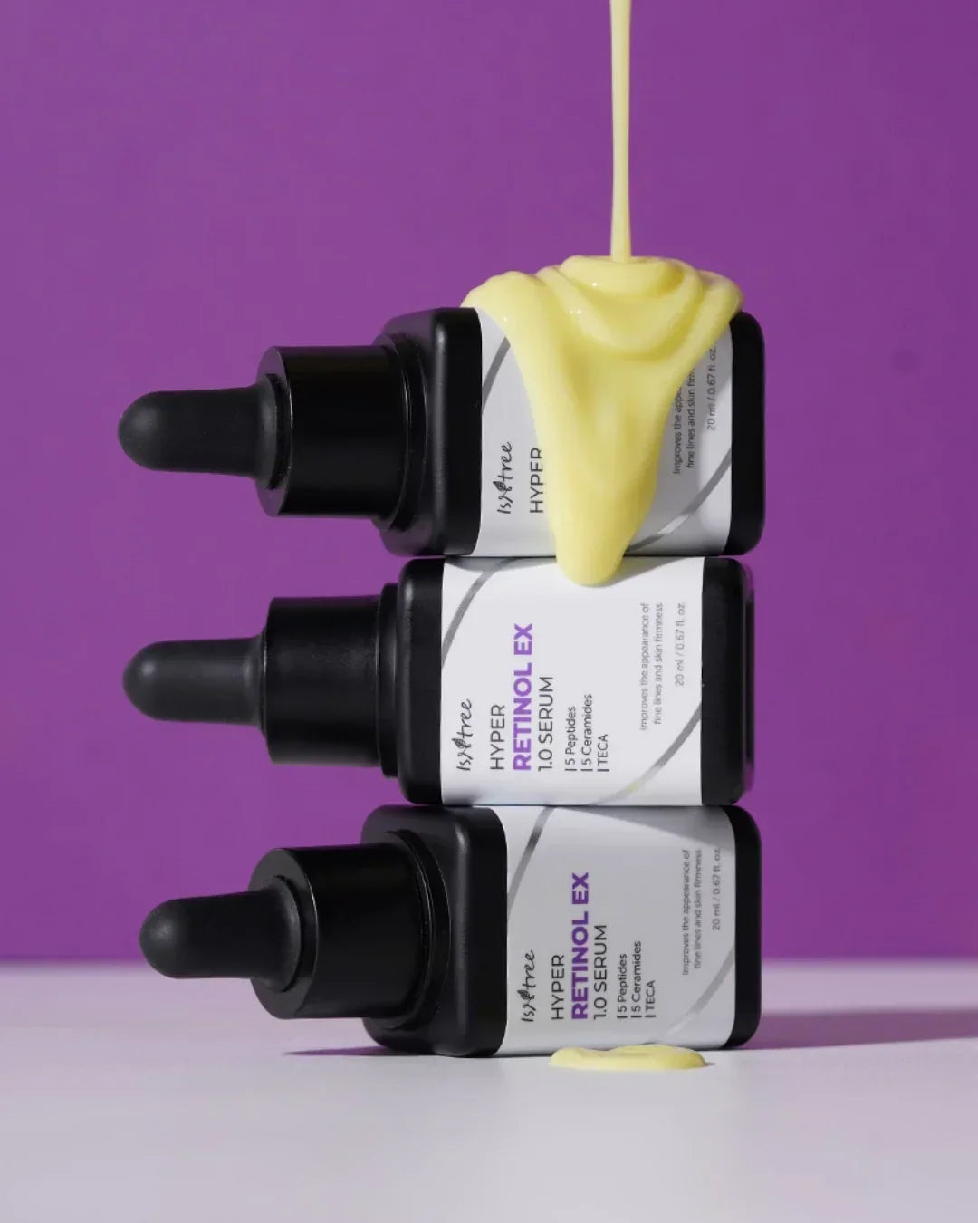 Stacked Isntree Hyper Retinol EX 1.0 Serum bottles with yellow serum dripping and purple background