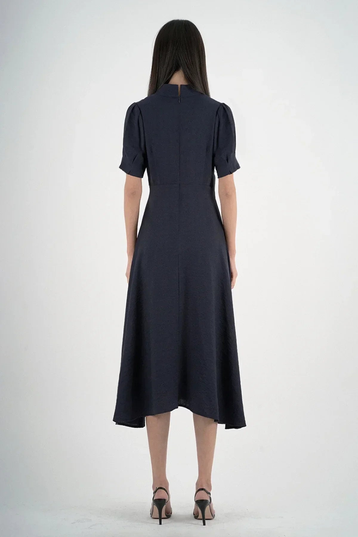Back view of woman wearing navy blue midi dress with short puff sleeves and black high heels