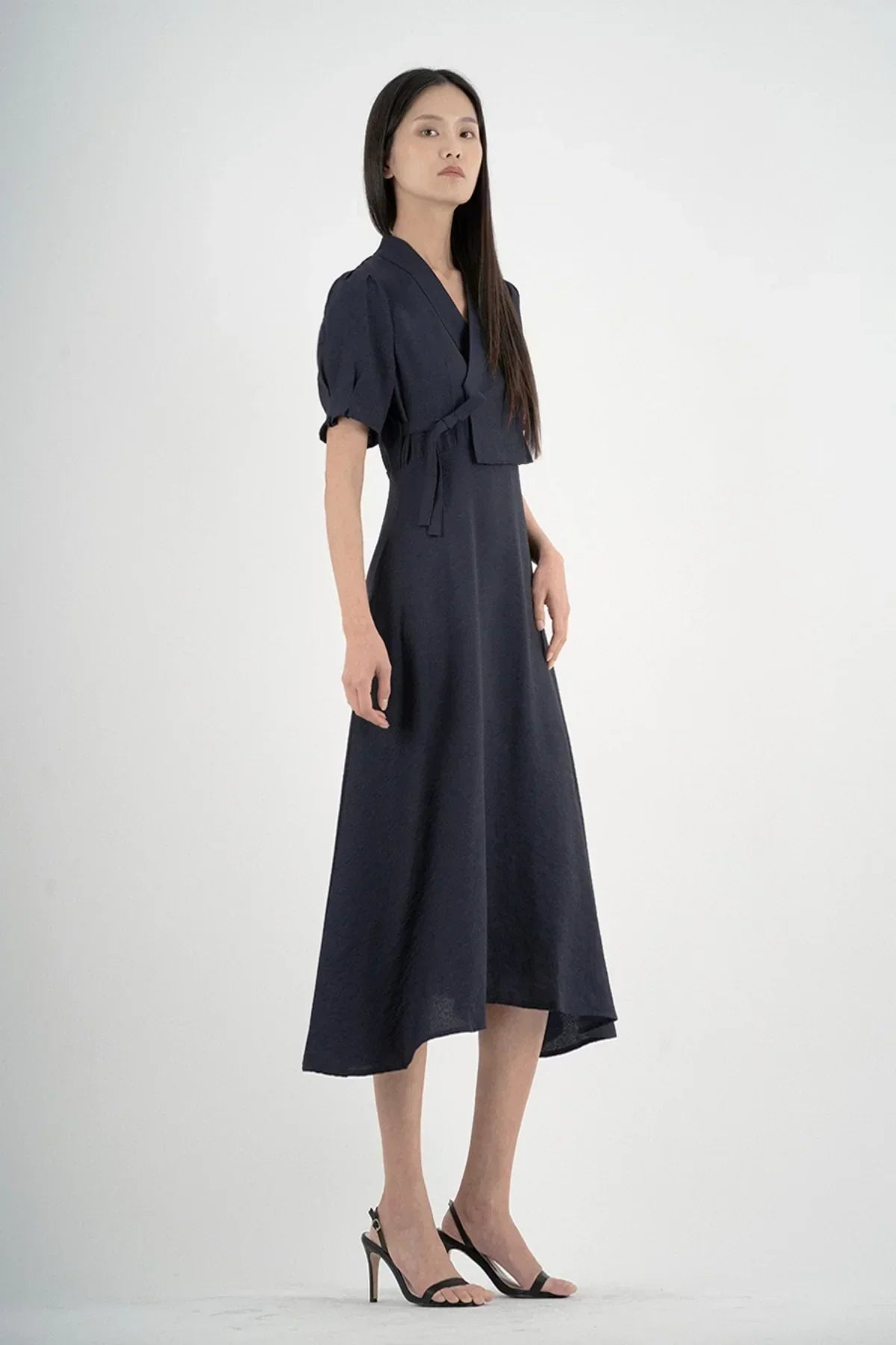 Model wearing navy blue midi dress with puff sleeves and wrap detail in studio