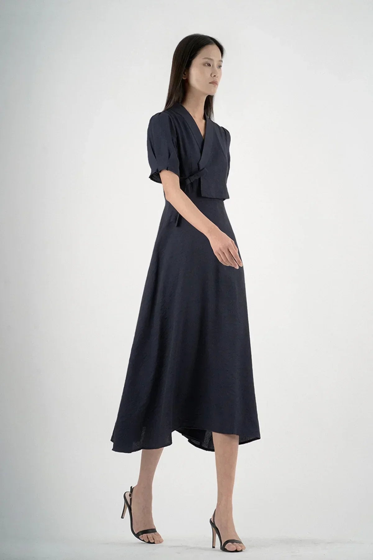 Woman wearing a navy wrap dress with short puff sleeves and black high-heeled sandals in studio
