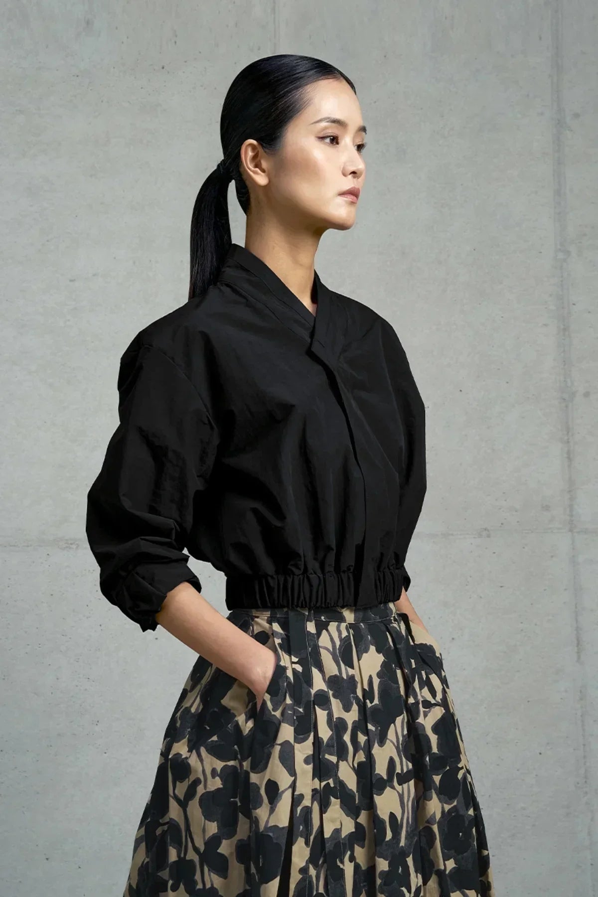 Woman wearing black cropped jacket and beige floral print skirt with hands in pockets