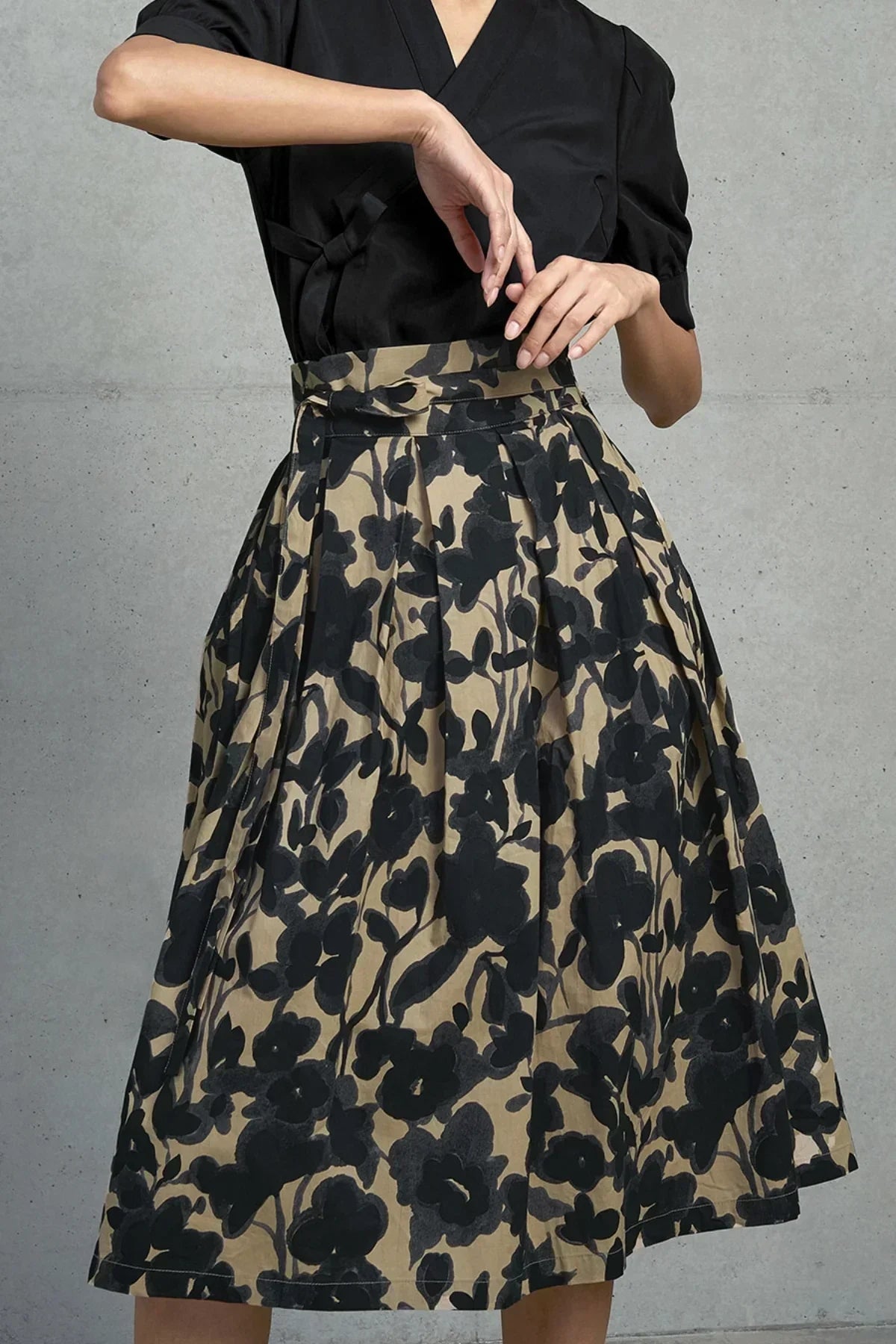 Beige skirt with black floral ink wash print paired with black top on model against gray background