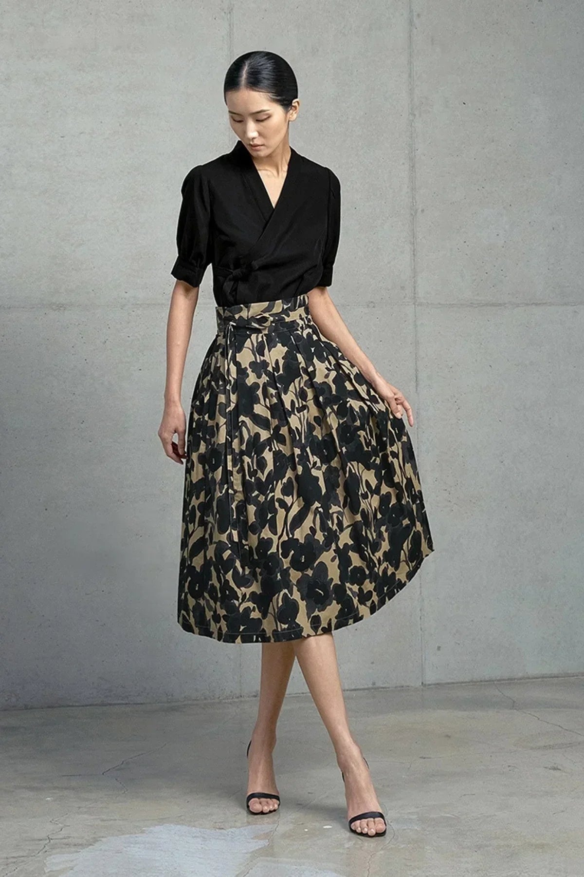 Woman wearing black blouse and high-waisted beige skirt with black floral print in minimalist studio