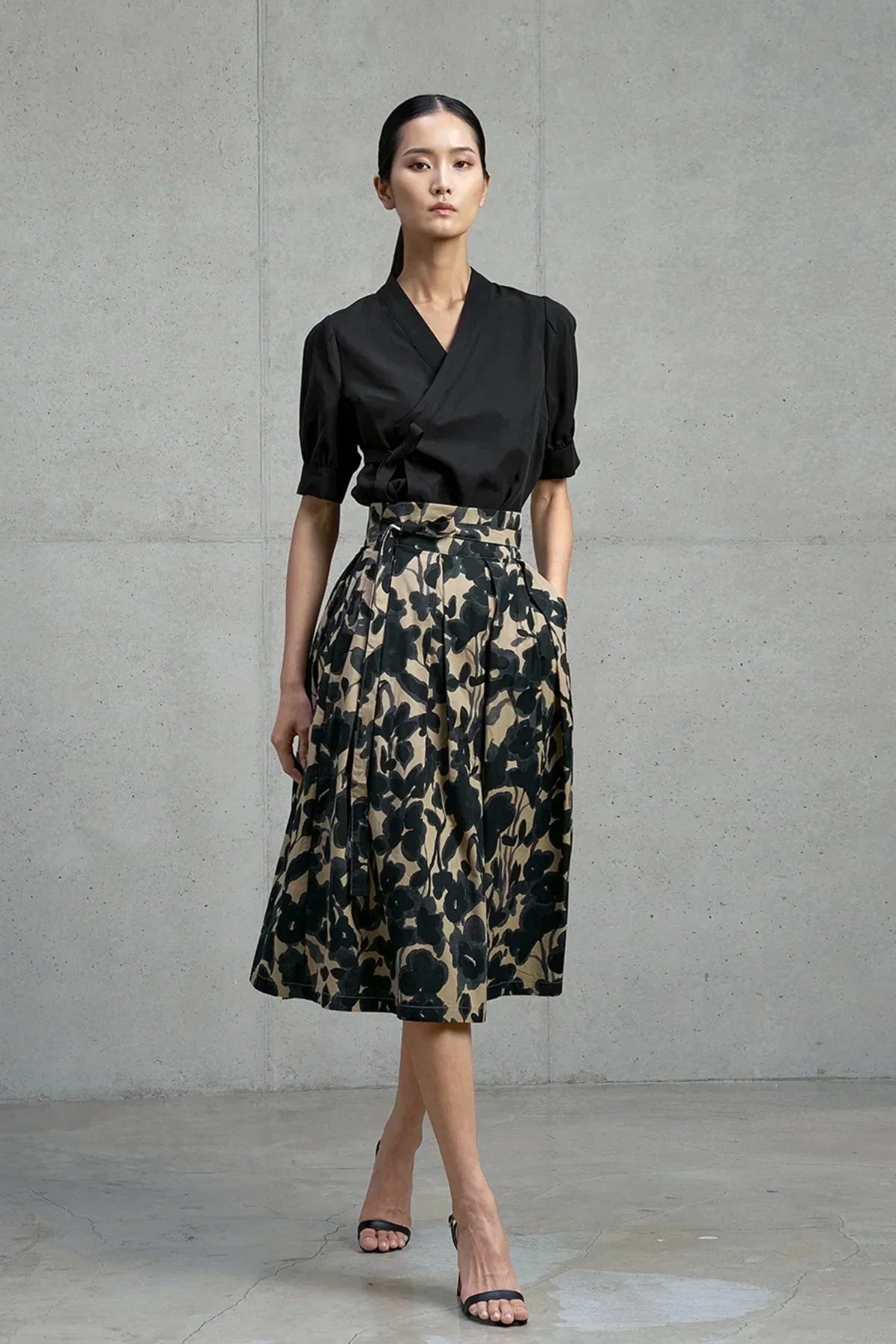 Woman wearing black wrap top and beige skirt with black floral ink wash print against concrete wall