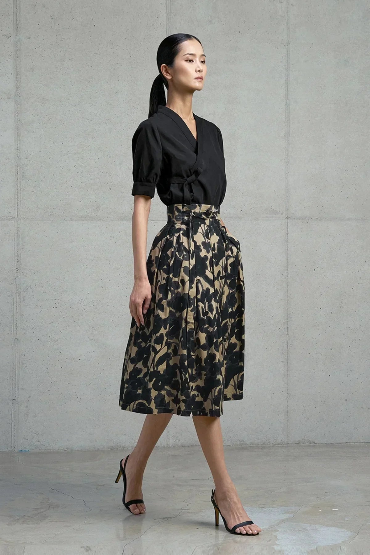 Woman wearing black wrap blouse and high-waisted floral print midi skirt with black heels