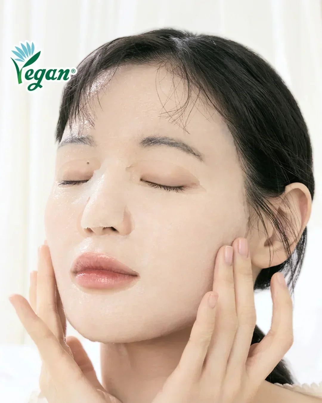 Woman applying vegan dewy jelly face mask with closed eyes and glowing skin