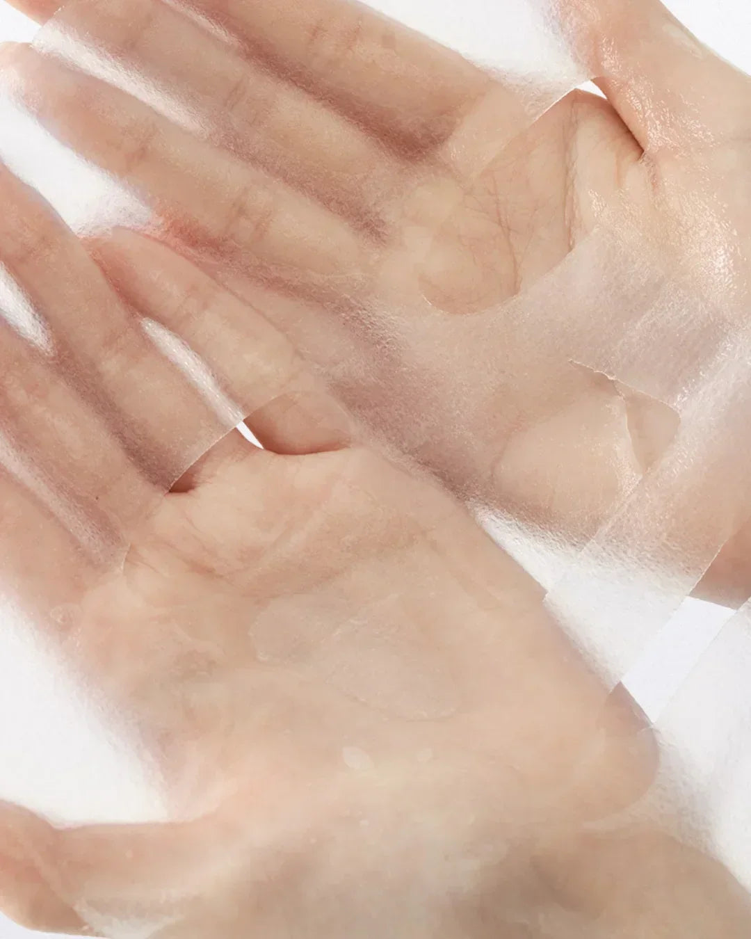 Close-up of hands holding translucent, dewy jelly face mask sheet with smooth texture