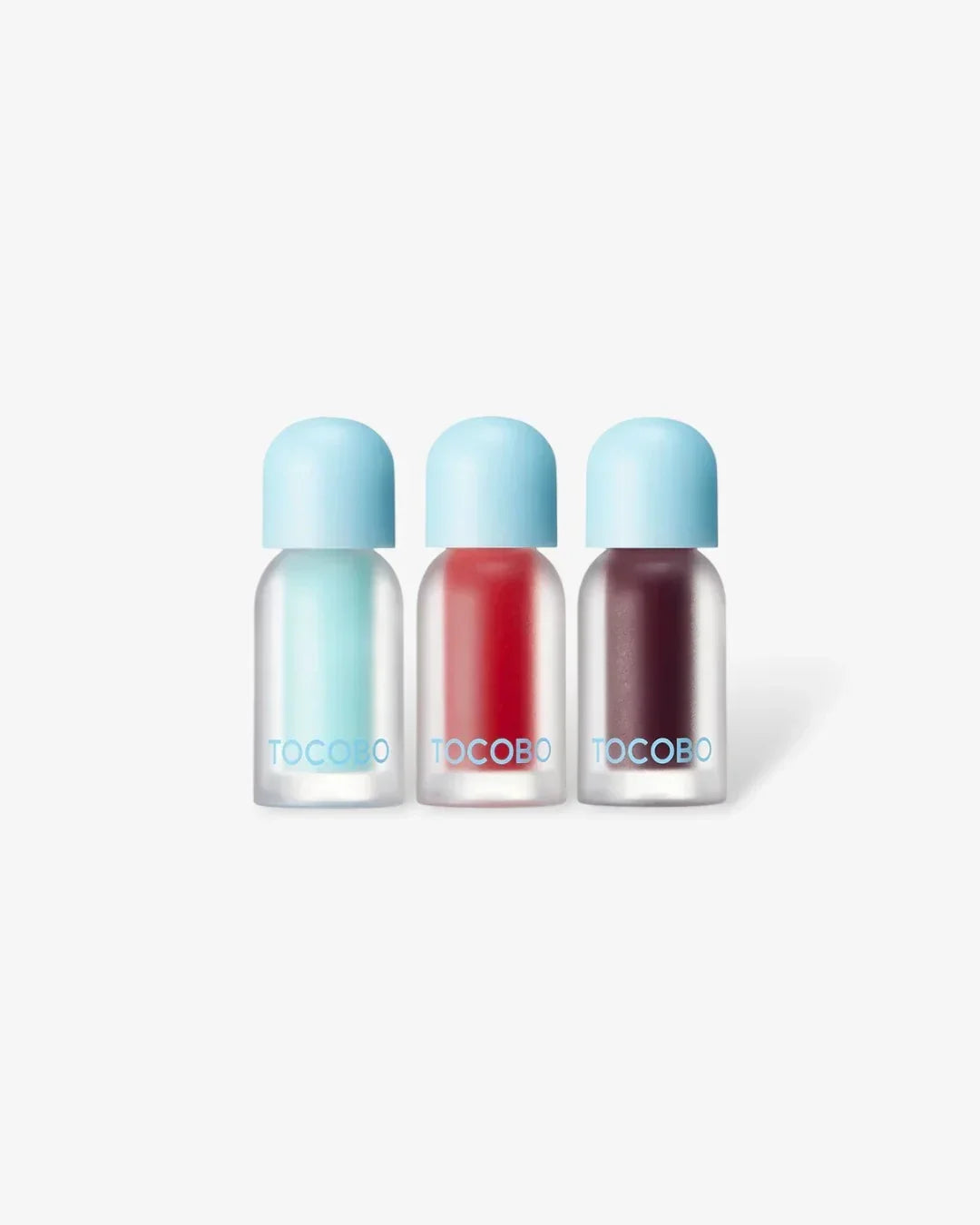 Three TOCOBO lip plumping oils in blue, red, and dark berry shades with light blue caps on a white background