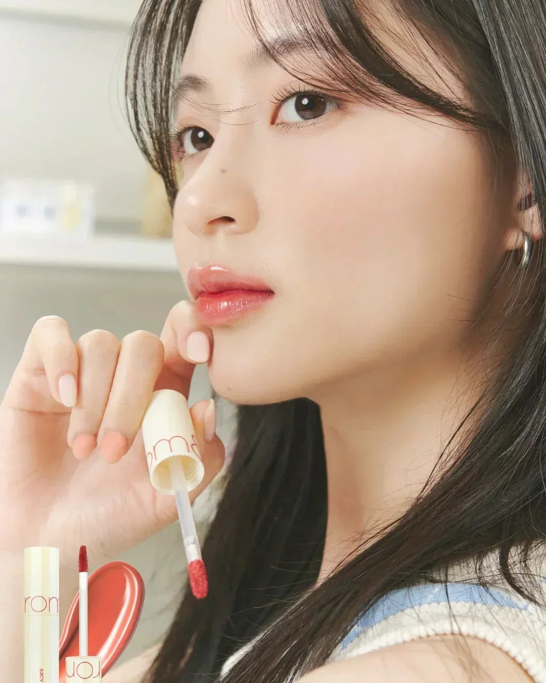 Close-up of woman applying red juicy lasting tint lip gloss with smooth skin and dark hair