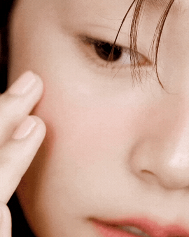 Close-up of a woman applying pink lip and cheek balm to her cheek with fingers, soft natural makeup
