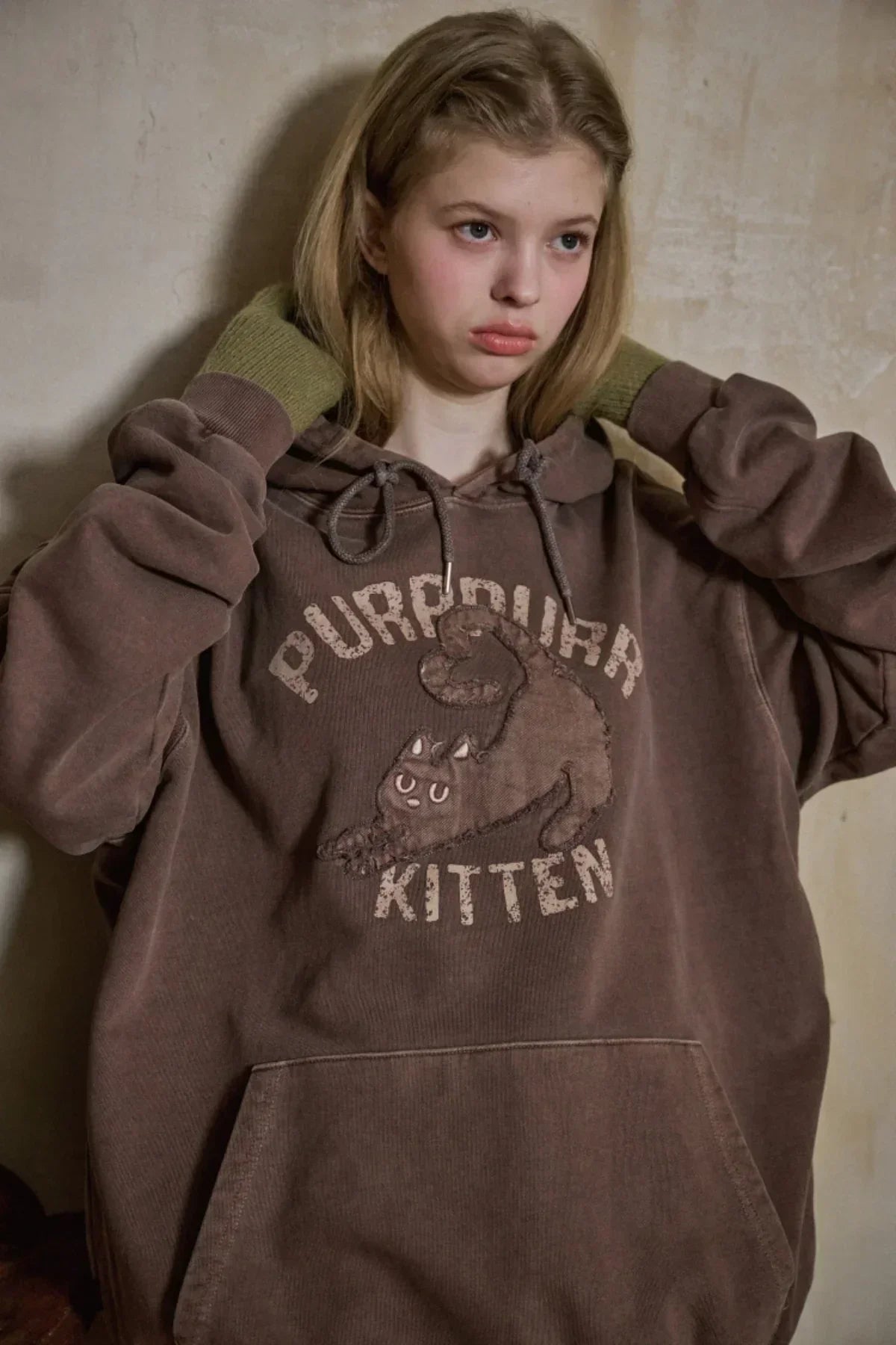 Young woman wearing brown oversized hoodie with kitten graphic and PURPUR KITTEN text