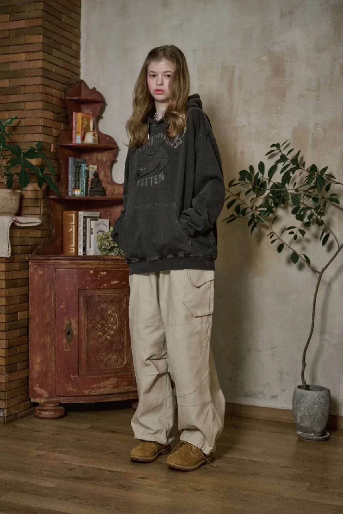 Young woman wearing oversized smoke black kitten print hoodie and beige cargo pants indoors with wooden floor