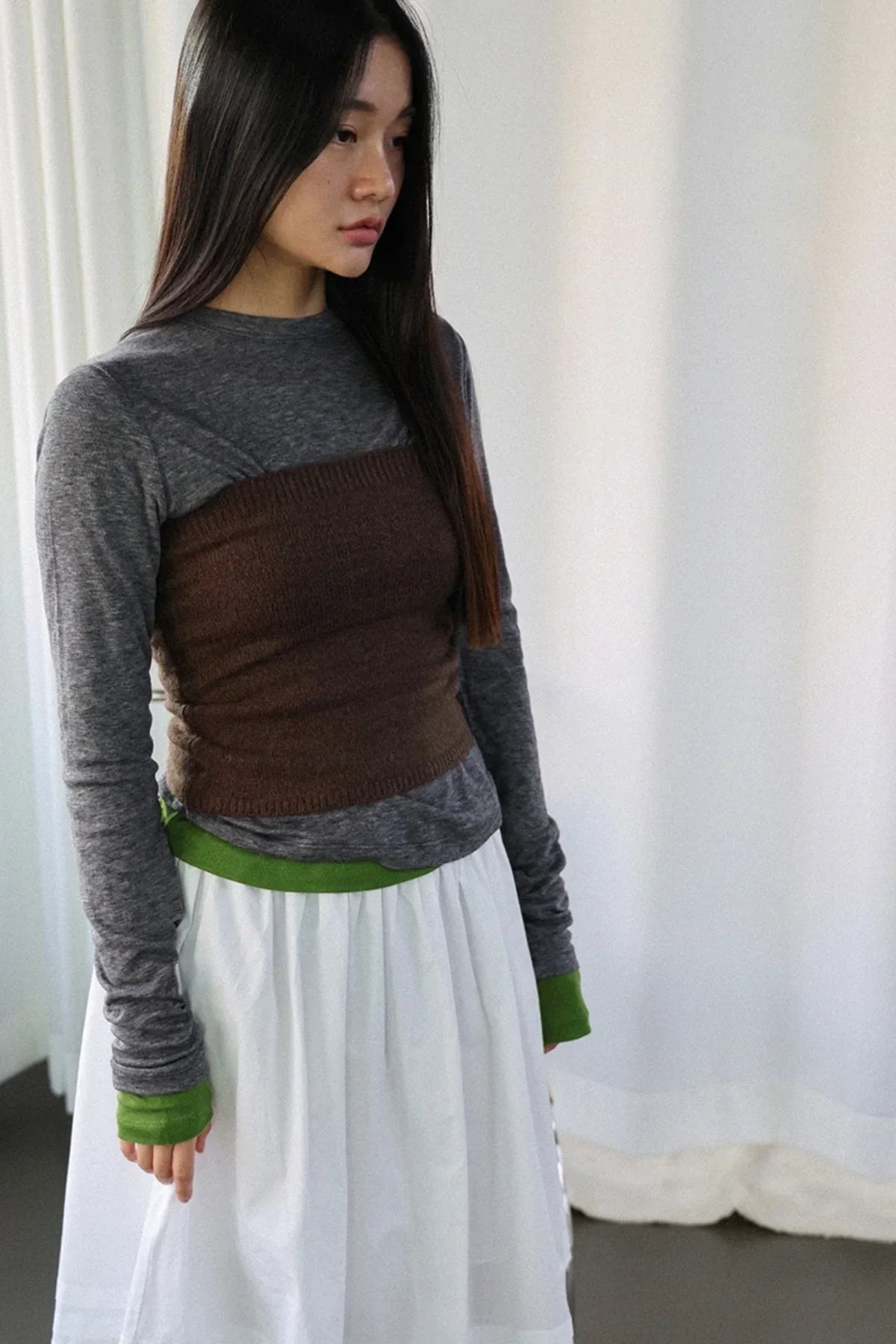 Woman wearing layered outfit with brown knit tube top over gray long sleeve shirt and white skirt