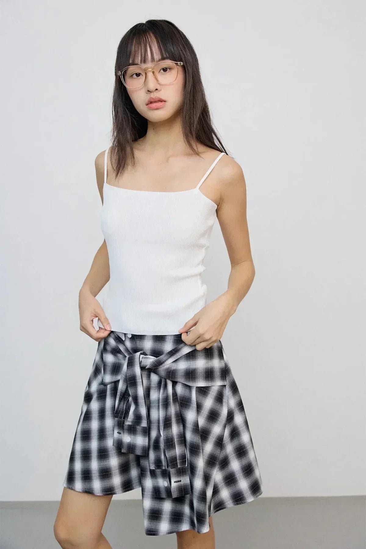 Young woman in beige glasses wearing a white tank top and black-and-white checkered skirt with tied shirt detail