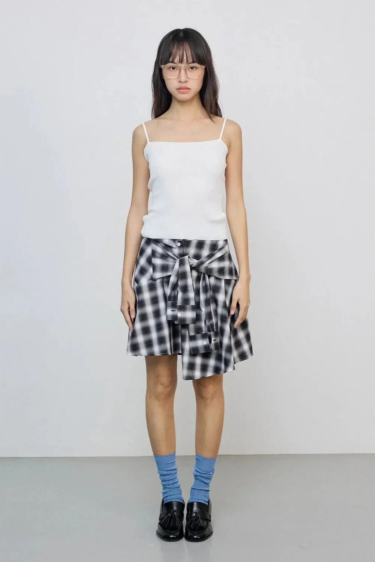 woman wearing white spaghetti strap top with black checkered skirt tied at waist and blue socks