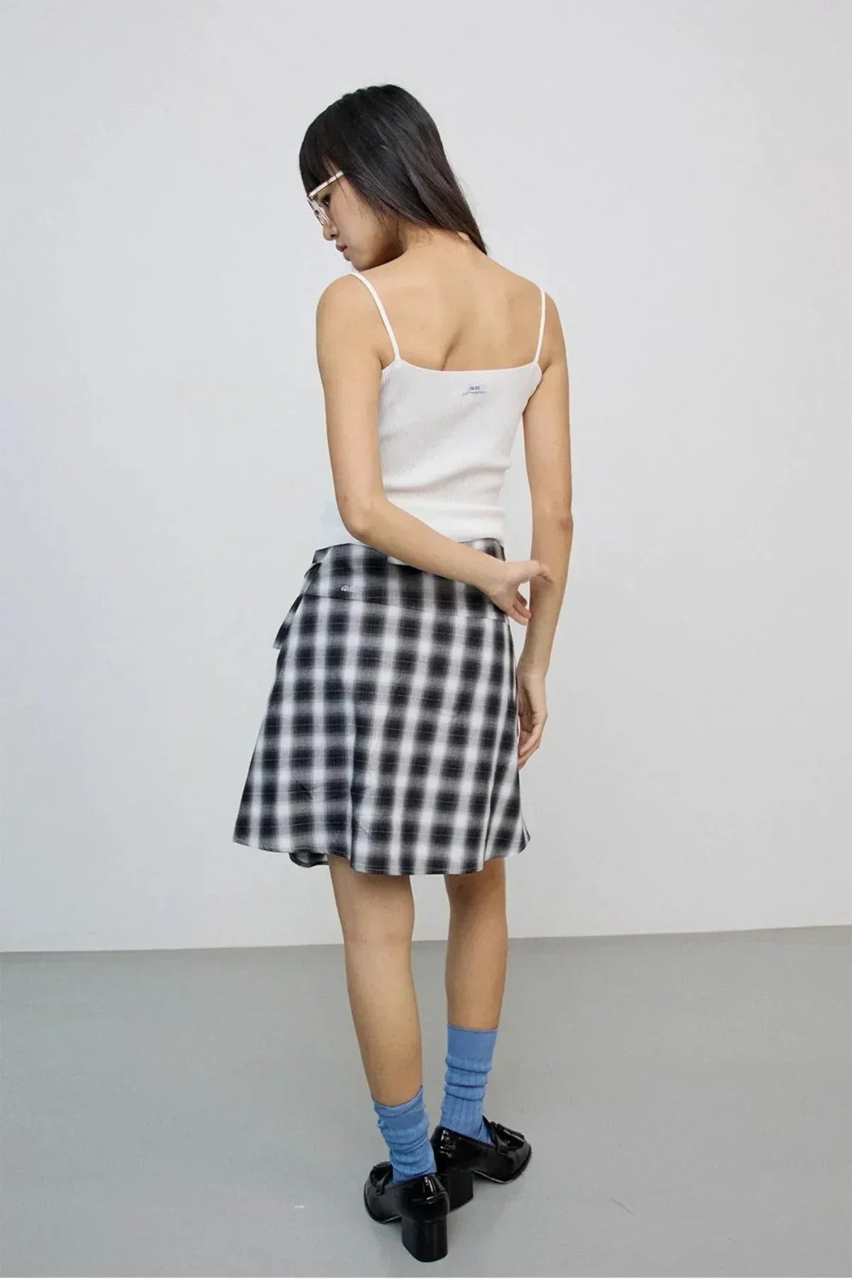 Woman wearing white spaghetti top and black-and-white checkered skirt with blue socks and black heels