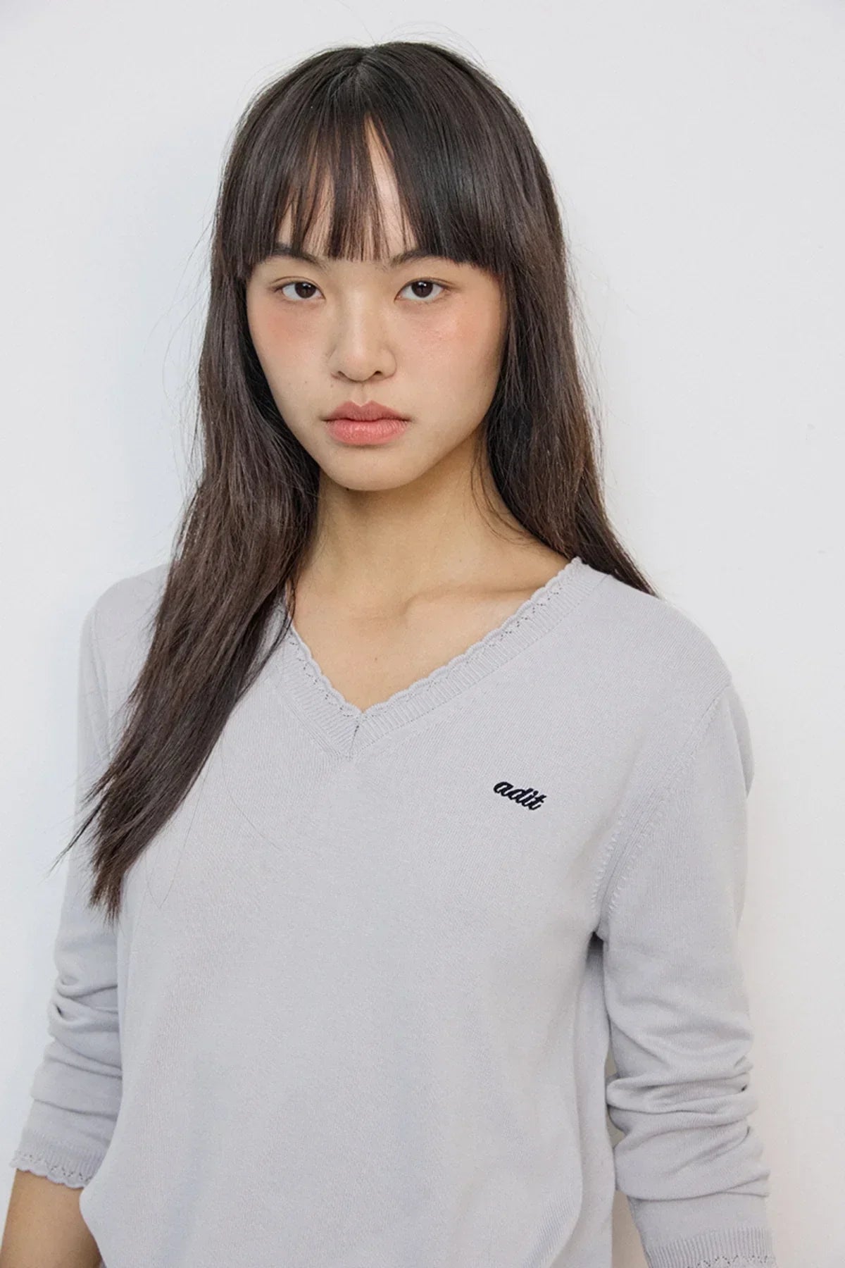Young woman wearing a light gray lace V-neck knit sweater with 3/4 sleeves and embroidered text on chest