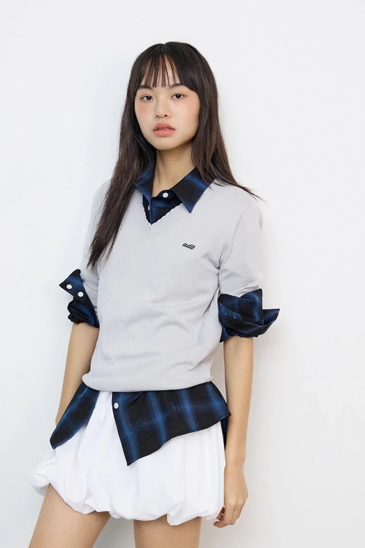 Young woman wearing gray lace V-neck knit sweater over navy blue plaid shirt and white skirt