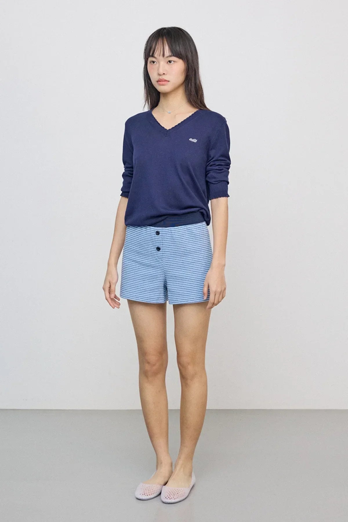 Woman wearing navy blue lace v-neck knit sweater and blue striped high-waist shorts in studio