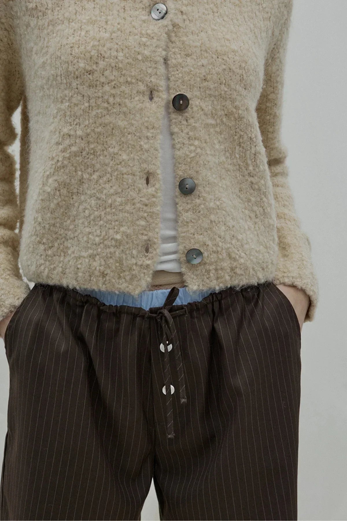 Close-up of person wearing beige fuzzy cardigan with buttons and dark pinstriped drawstring pants