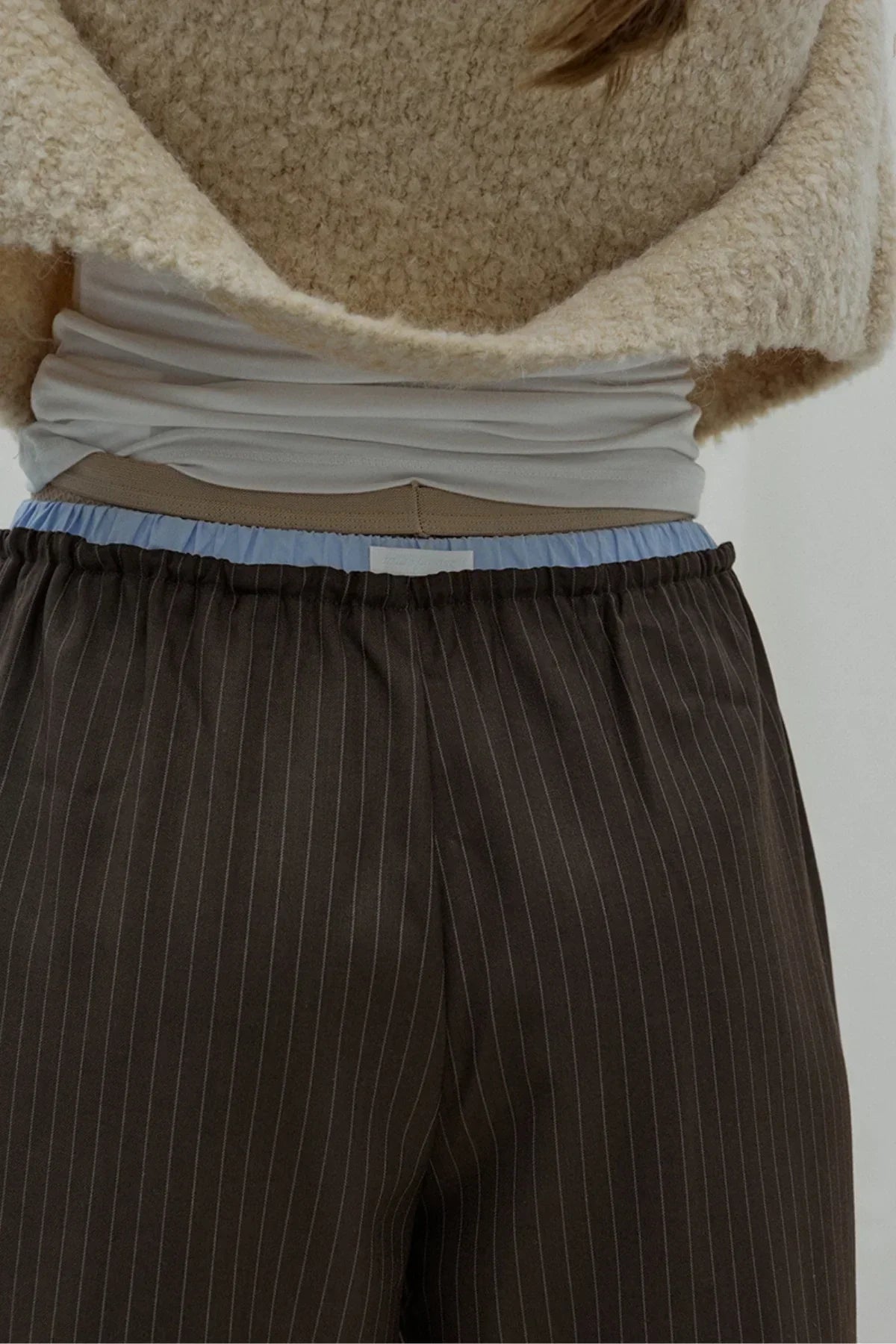 Close-up of brown pinstriped bermuda pants with layered light blue and beige waistbands and cream textured sweater