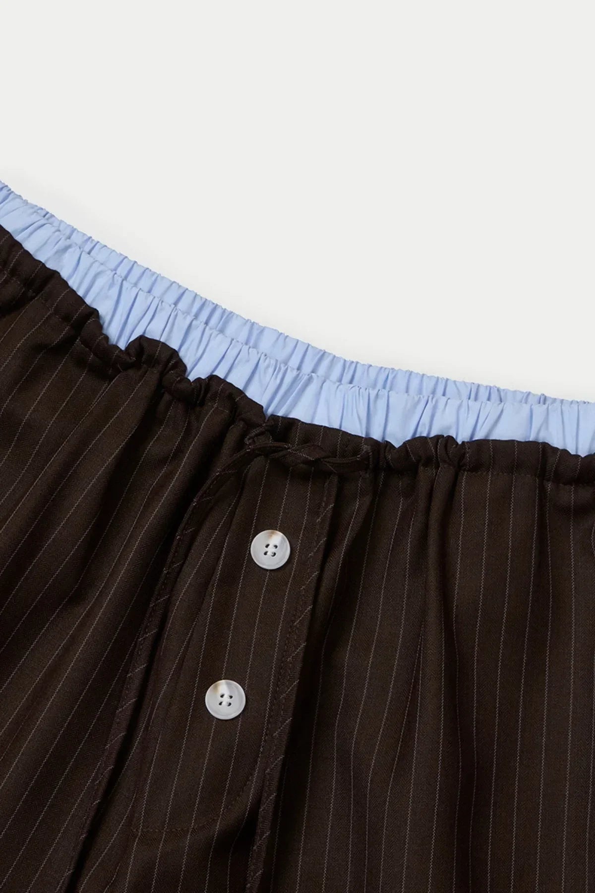 Close-up of brown pinstriped layered Bermuda pants with light blue elastic waistband and white buttons