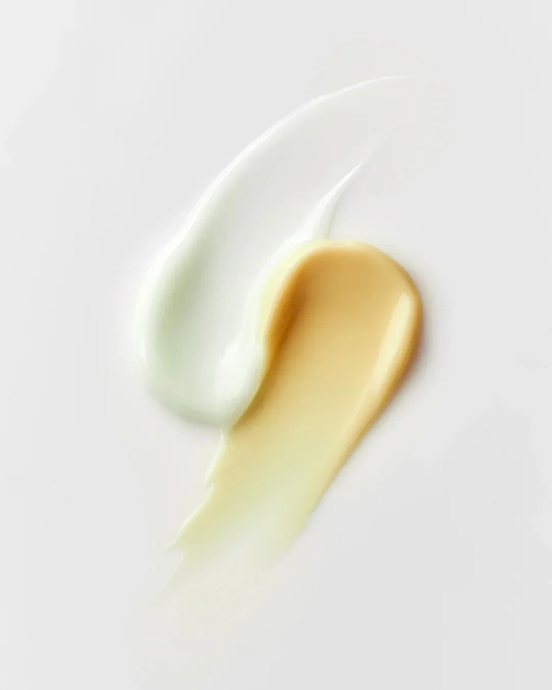 Two skincare serum textures smeared on white surface, one light green and one beige