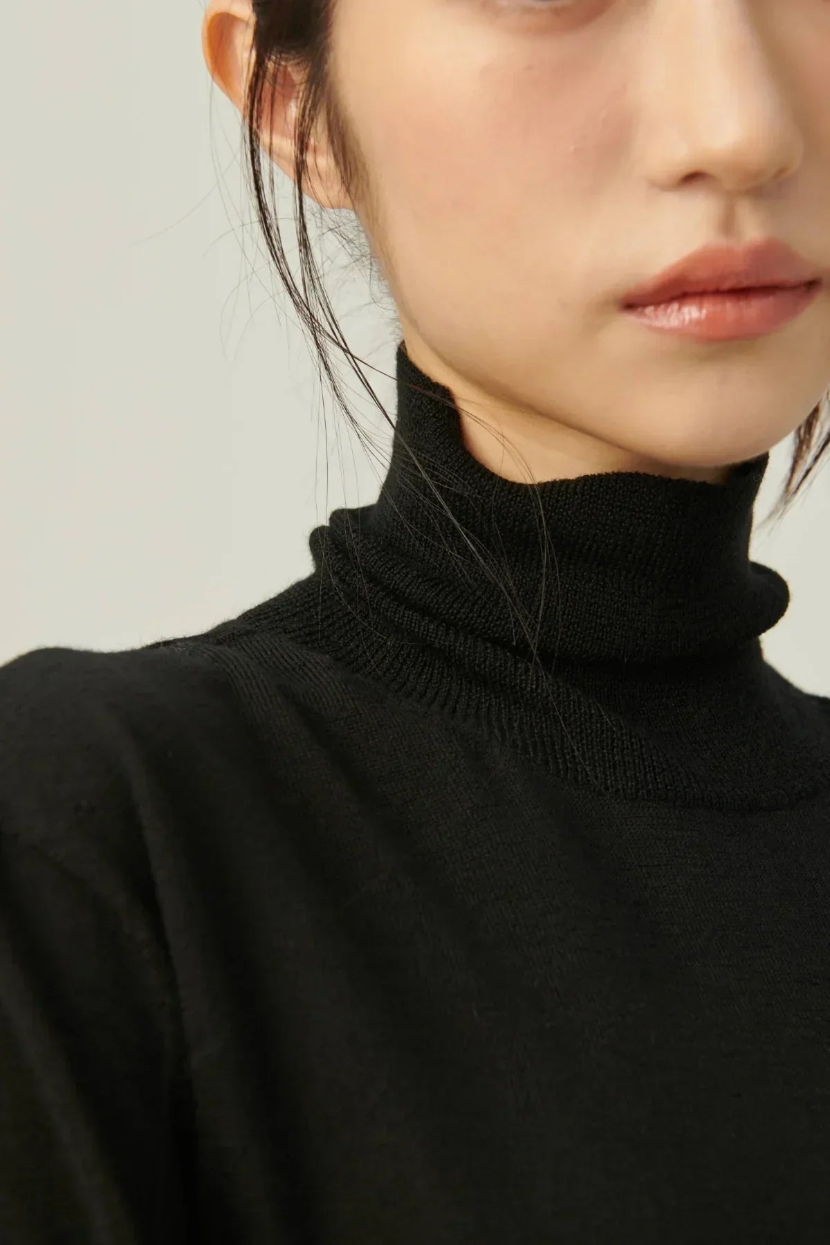 Close-up of a woman wearing a black lightweight knit turtleneck sweater with natural makeup