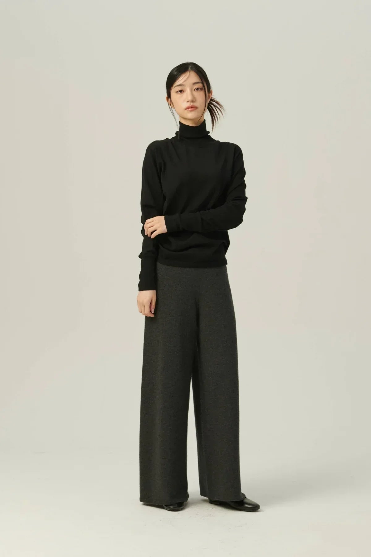Young woman wearing a black lightweight turtleneck knit sweater and wide-leg charcoal pants in studio