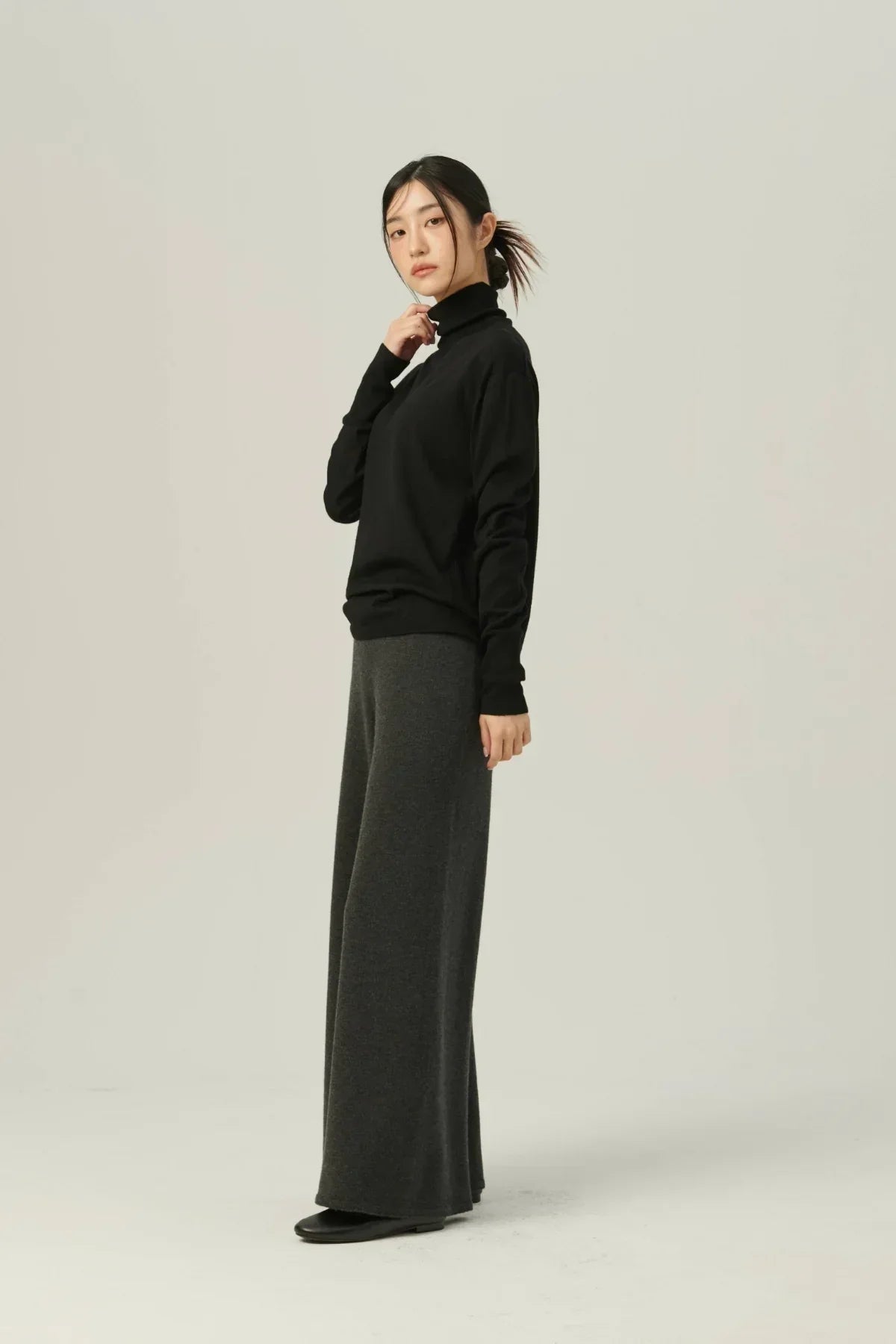 Woman wearing a black lightweight turtleneck knit and wide-leg gray pants on a plain background