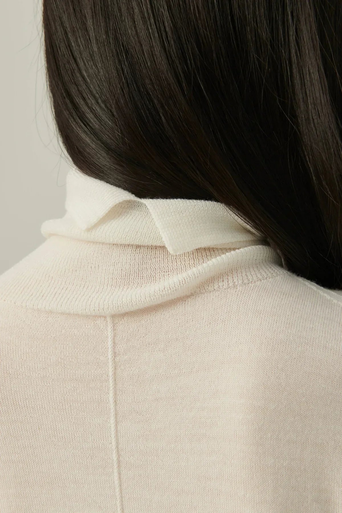Close-up of a person wearing a lightweight white turtleneck knit sweater with dark hair