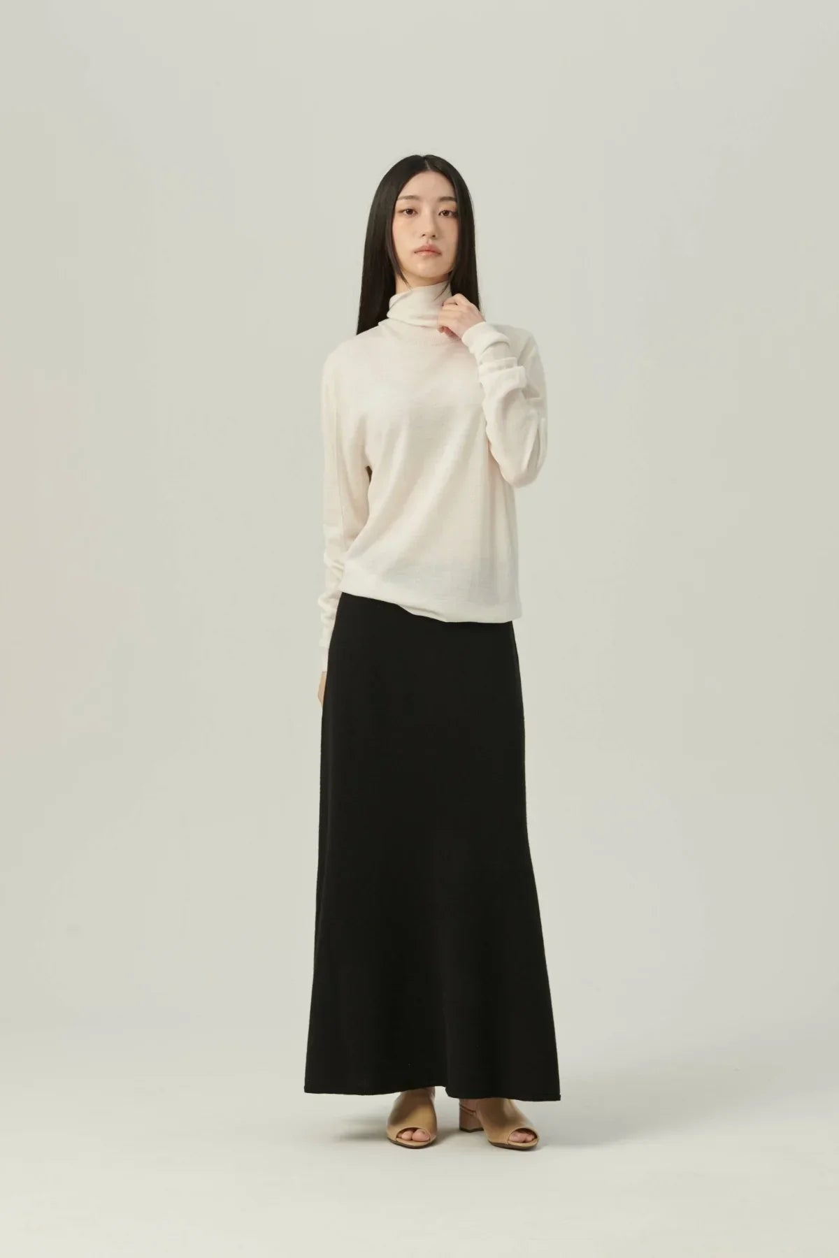 Woman wearing a lightweight white turtleneck knit sweater and a long black skirt with beige open-toe heels