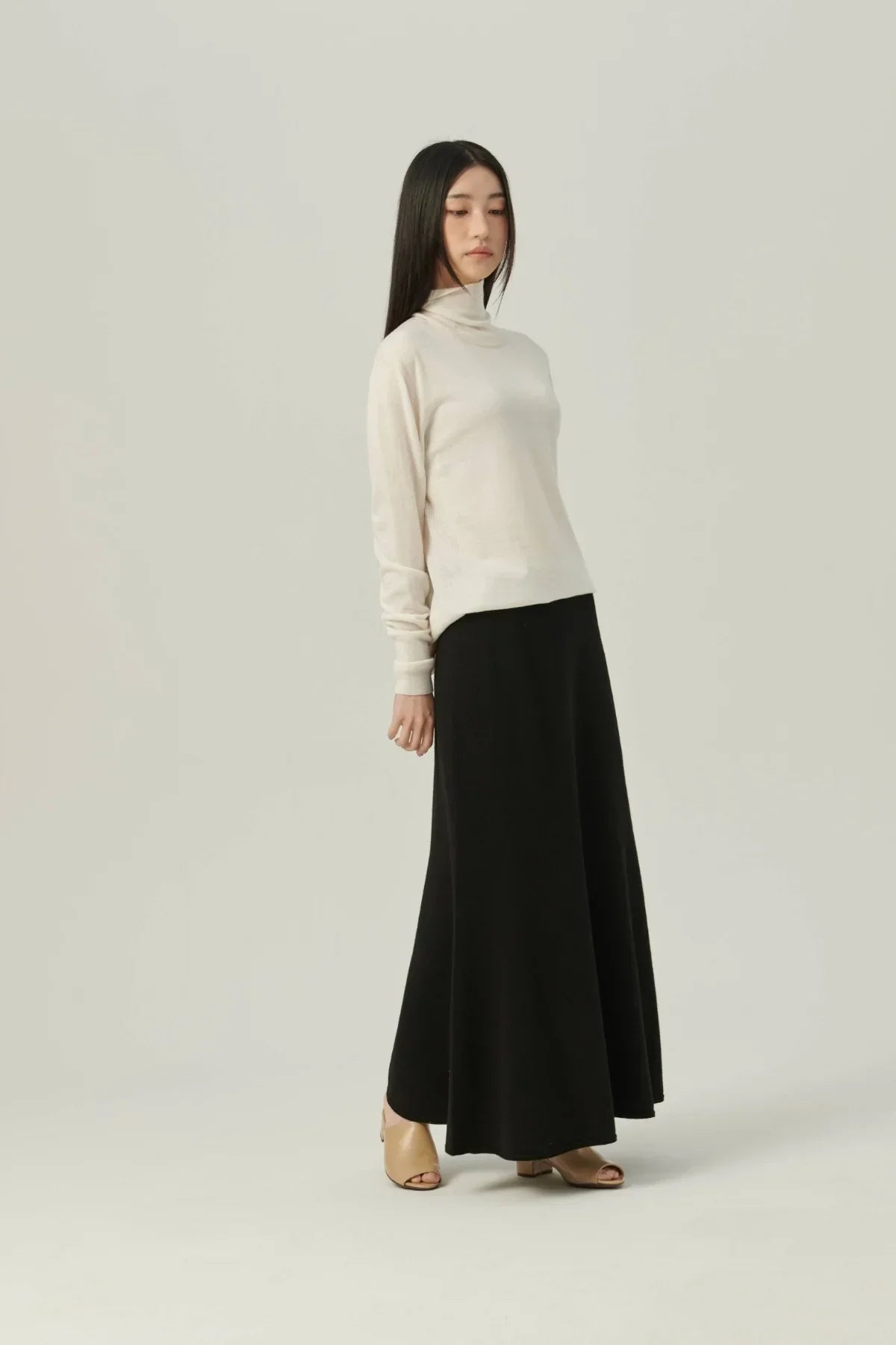 Woman wearing a white lightweight turtleneck knit sweater paired with a long black skirt and beige open-toe heels