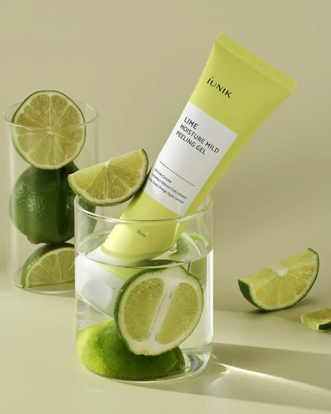 iUNIK Lime Moisture Mild Peeling Gel tube in glass with water and fresh lime slices on beige background