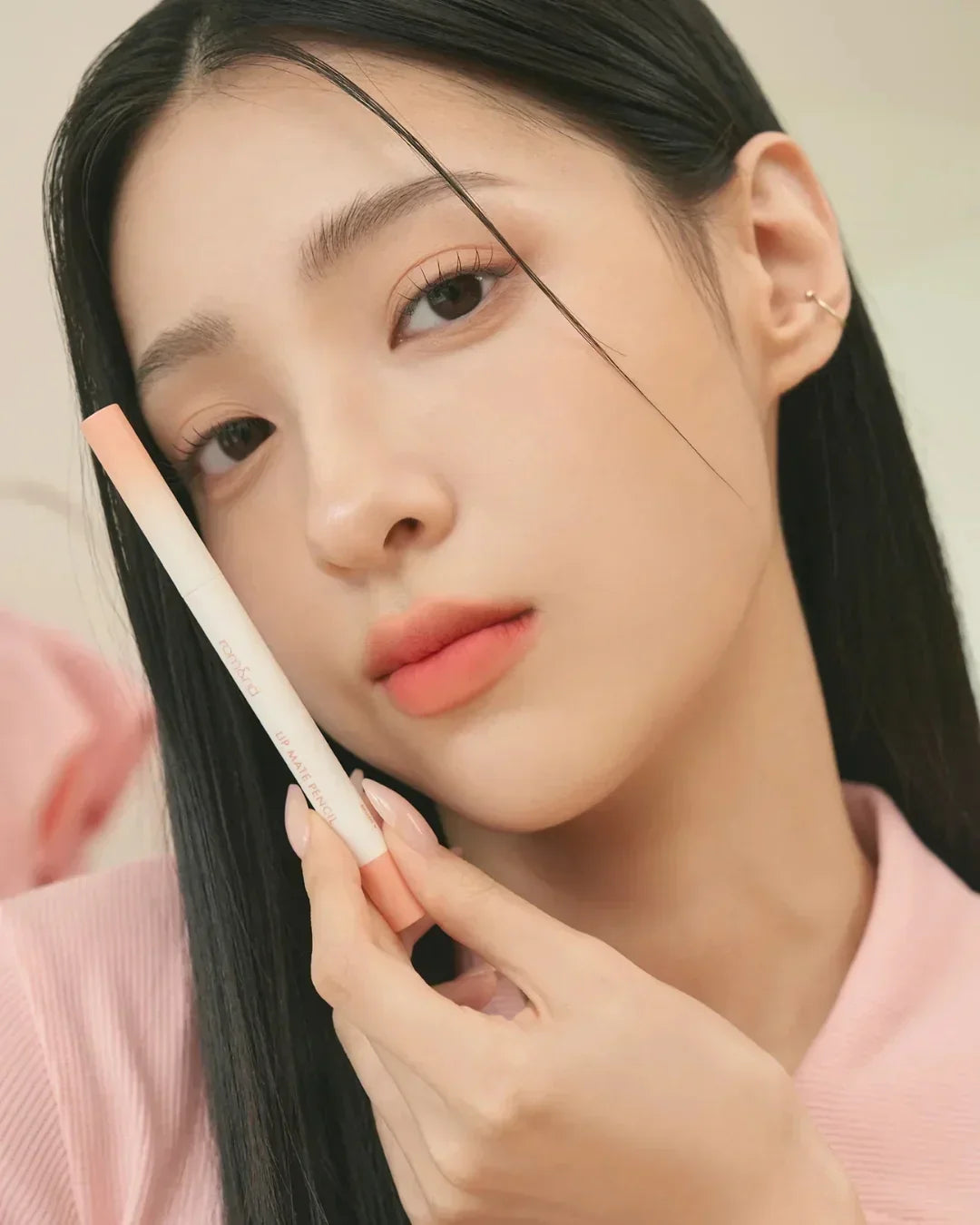 Close-up of woman with natural makeup holding Rom&nd Lip Mate Pencil in soft pink shade